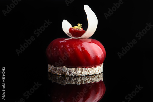 Round cake in red glaze decorated with pieces of coconut on a black background..