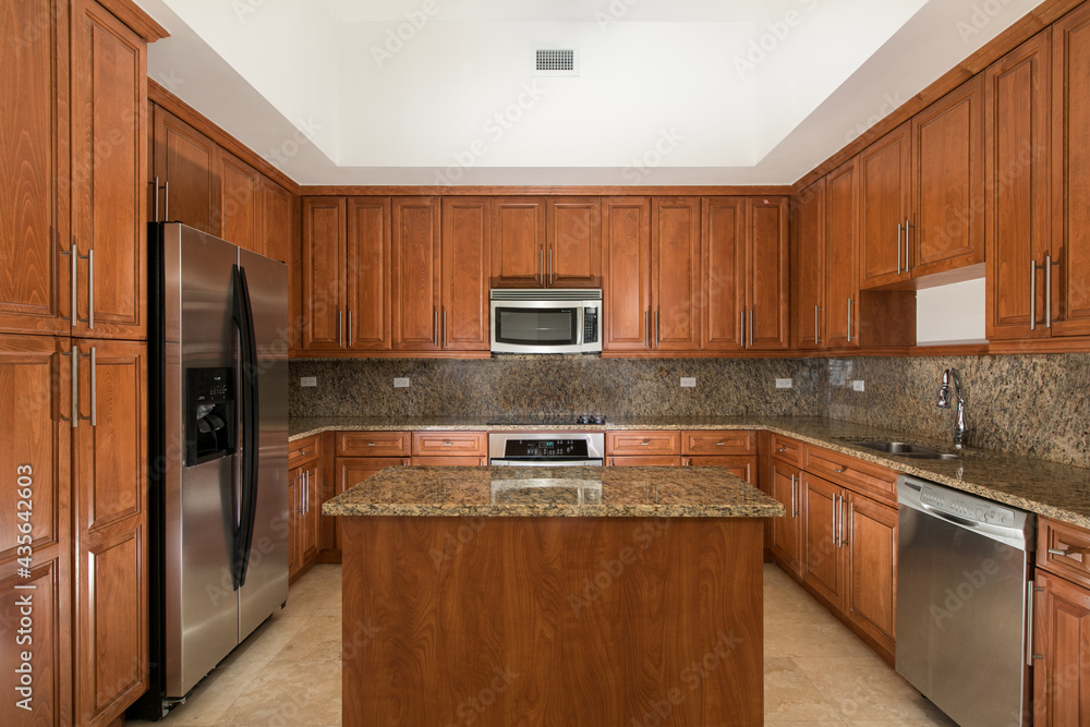 Fototapeta premium Vacant Kitchen with cherry wood cabinets and center island with granite.