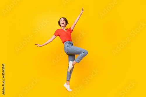 Full size photo of cheerful girl look empty space raise hand knee have good mood isolated on yellow color background