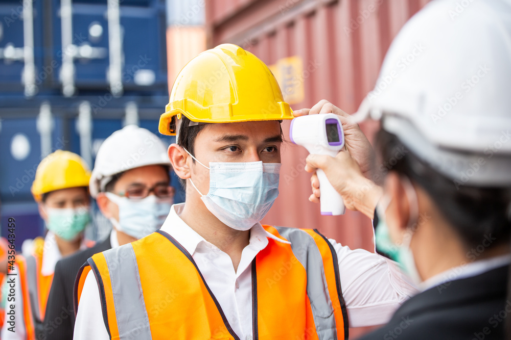 Female worker scanning fever temperature with digital thermometer to construction site staff wearing hygiene face mask protect from Coronavirus or COVID-19. New Normal working Female worker scanning fever temperature with digital thermometer to construction site staff wearing hygiene face mask protect from Coronavirus or COVID-19. New Normal working