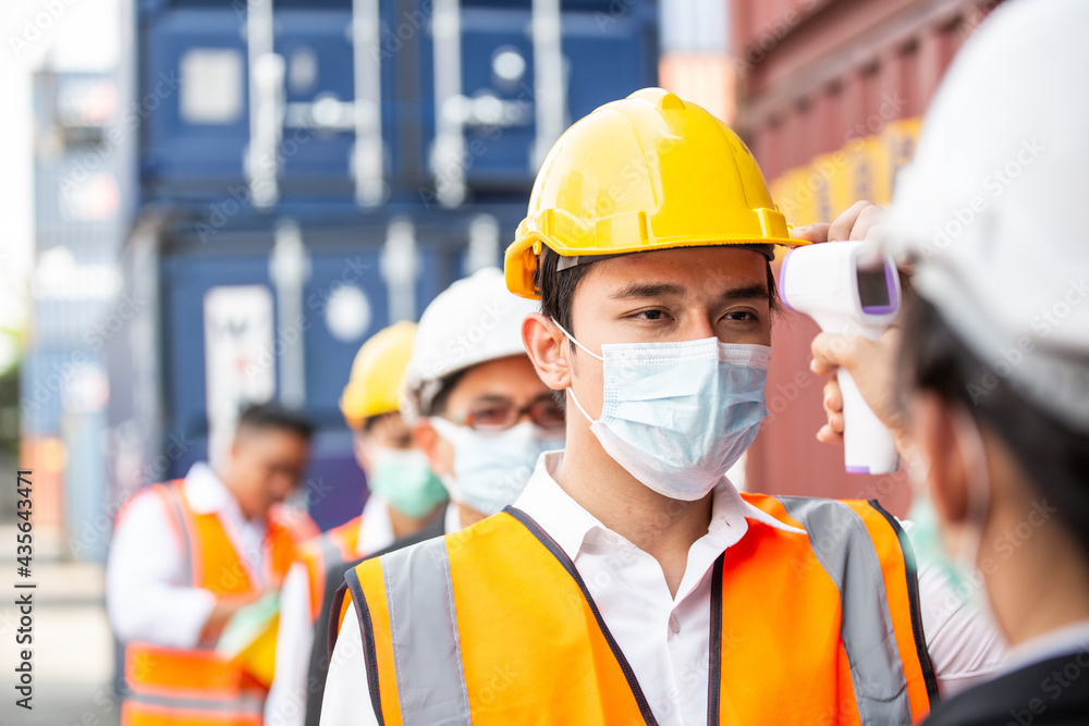 Female worker scanning fever temperature with digital thermometer to construction site staff wearing hygiene face mask protect from Coronavirus or COVID-19. New Normal working Female worker scanning fever temperature with digital thermometer to construction site staff wearing hygiene face mask protect from Coronavirus or COVID-19. New Normal working