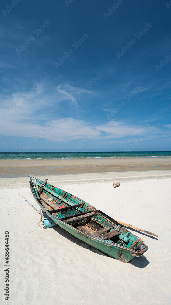 A fishing boat moored on a white sandy beach by the sea with beautiful sky With a harbor in the background