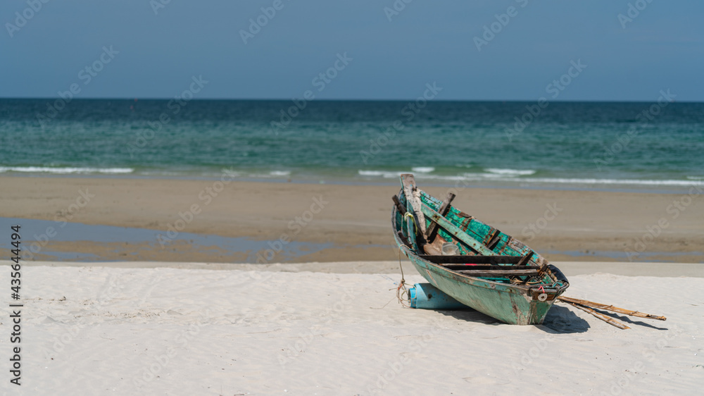 A fishing boat moored on a white sandy beach by the sea with a beautiful sky.