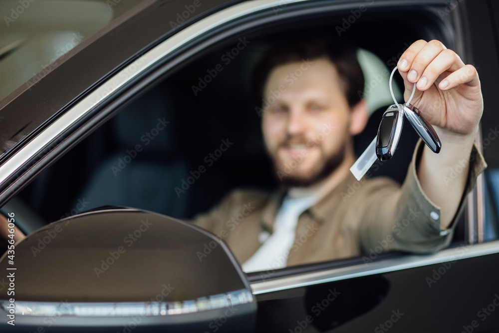 Happy man showing a car key inside his new vehicle, focus on hand. Male customer with car key sitting in new modern car.