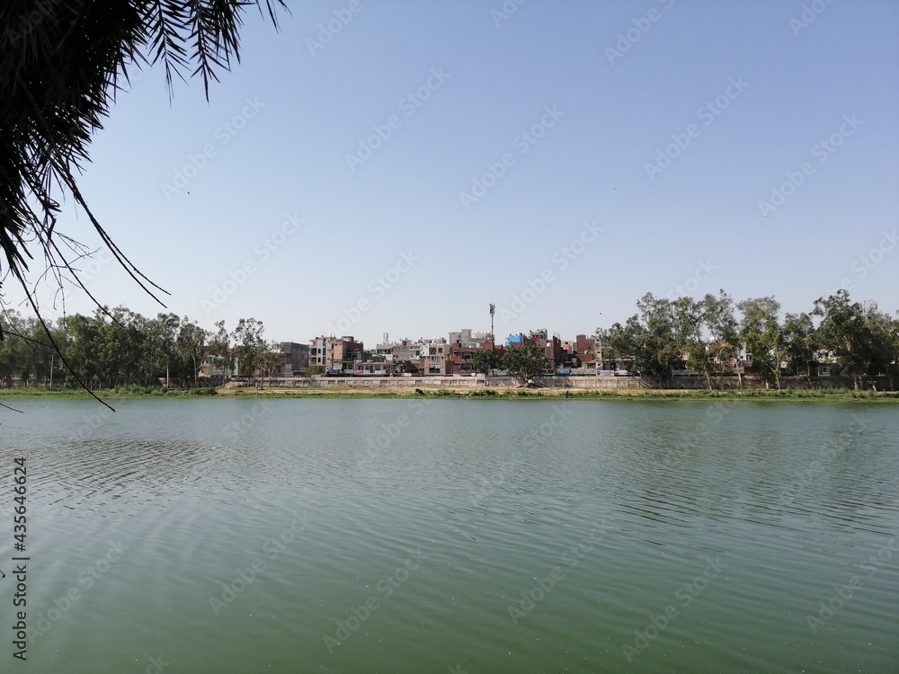 Sanjay Lake in Turquoise color against blue sky with trees in the background in East Delhi in India Sanjay Lake in Turquoise color against blue sky with trees in the background in East Delhi in India