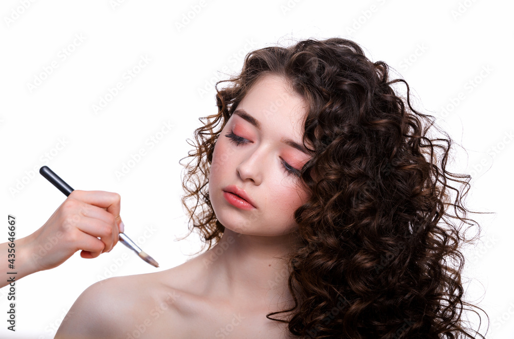 Obraz premium Make-up artist smoothes skin tone on body beautiful young woman in the beauty salon makes a hair curling and makeup
