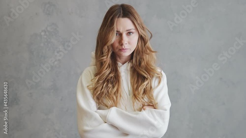 The offended woman in hoodie looking at the camera and shaking her head negatively while standing in a gray studio