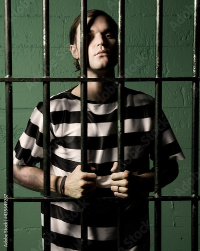 Man in striped clothes in prison cell holding bars wishing to be free photo