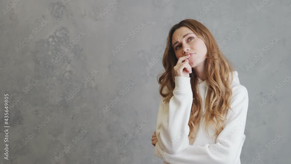 A brooding woman in a hoodie founding a good option for herself while standing in a gray studio A brooding woman in a hoodie founding a good option for herself while standing in a gray studio