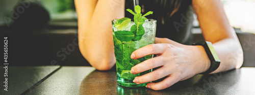 young woman's hand holding a glass with mohito lemonade cocktail in cafe