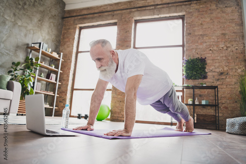 Full length photo of grey haired retired pensioner wear sportswear hold plank on mat indoors in house gym