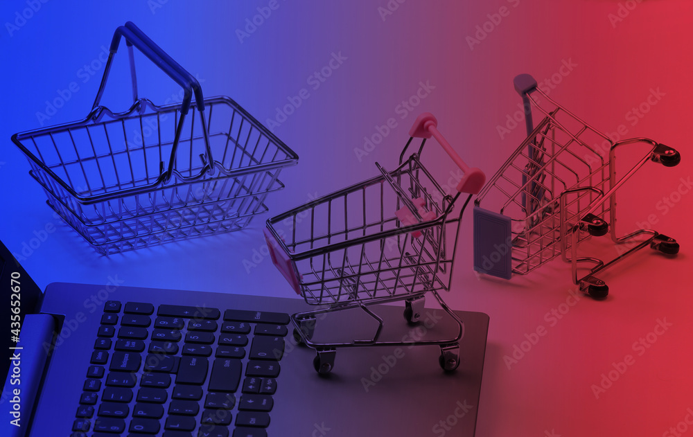 Online shopping. Laptop with supermarket trolleys, basket in neon light Online shopping. Laptop with supermarket trolleys, basket in neon light