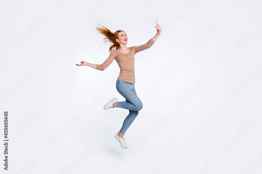 Full length photo of sweet funky redhair woman beige shirt jumping high tacking selfie modern device isolated white color background