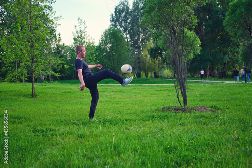 The guy kicks the ball on the grass in the summer park