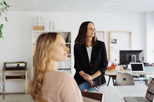 Two businesswoman sitting in a meeting looking to the side listening