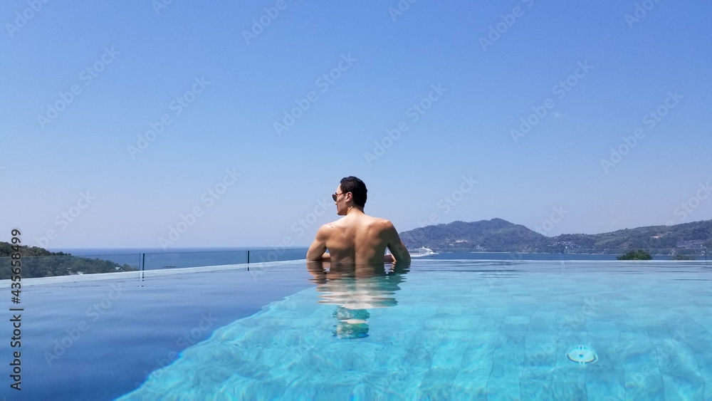 Muscular asian man relaxing in an infinity pool oceanside in a luxery resort sunbaking