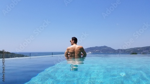 Muscular asian man relaxing in an infinity pool oceanside in a luxery resort sunbaking