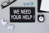 WE NEED YOUR HELP. informationon on a black notebook, on a background office table.