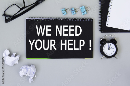 WE NEED YOUR HELP. informationon on a black notebook, on a background office table.