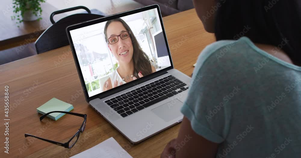 Mixed race businesswoman sitting at desk using laptop having video call with female colleague Mixed race businesswoman sitting at desk using laptop having video call with female colleague