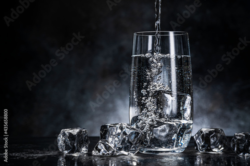 Pouring water from bottle into glass on black background