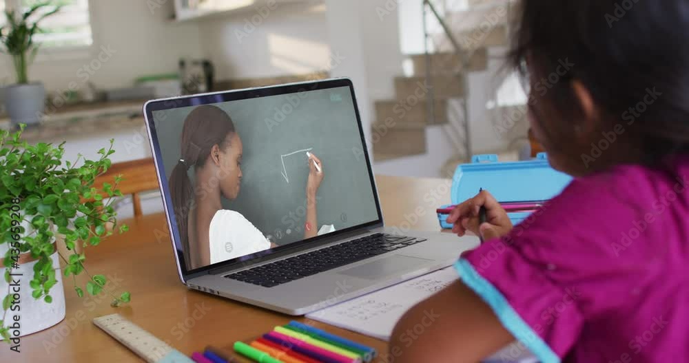 African american girl doing homework while having a video call with female teacher on laptop at home African american girl doing homework while having a video call with female teacher on laptop at home