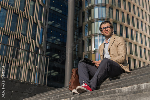 Young man in casual wear sitting on stairs near modern glass building © a_medvedkov