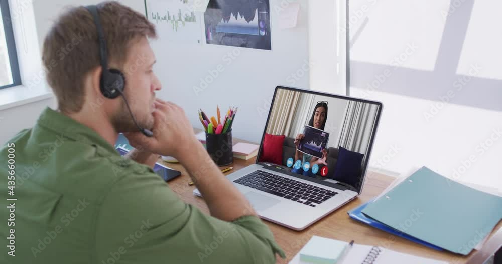 Caucasian man wearing phone headset having a video call with female colleague on laptop at office Caucasian man wearing phone headset having a video call with female colleague on laptop at office