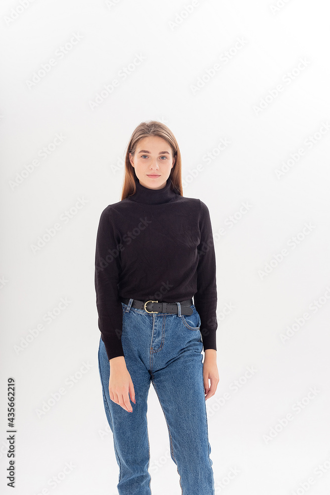 portrait of young attractive caucasian woman with long hair in black  turtleneck, blue jeans isolated on white studio background. skinny pretty  female posing on cyclorama. model tests of beautiful lady Stock Photo