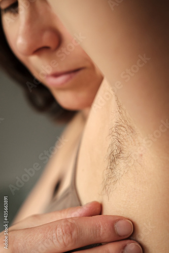 Hairy, unshaven female armpits on a blurred background of a female face. Concept of body positive and the adoption of its naturalness. 