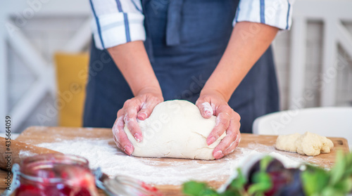 Female hands making dough. Dough with flour, eggs and other utensil, ingredients lies on white wooden table. Baking homemade process.