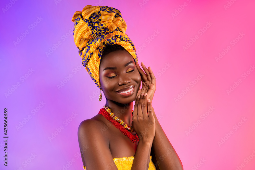 Photo of young happy dark skin lady wear tribal headwrap touch face hands isolated on vivid light background - obrazy, fototapety, plakaty 