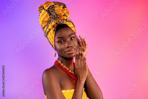 Photo of charming young afro american woman hold hands face wear tribal necklace isolated on vibrant background