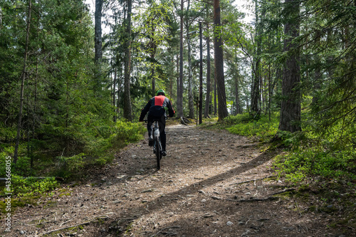 Man Cyclist on sport mountain bike on forest track. Male mountain bike racer cycling on trail with tree roots. Mountain biker rides in spring fresh air forest. Sports motivation and inspiration.