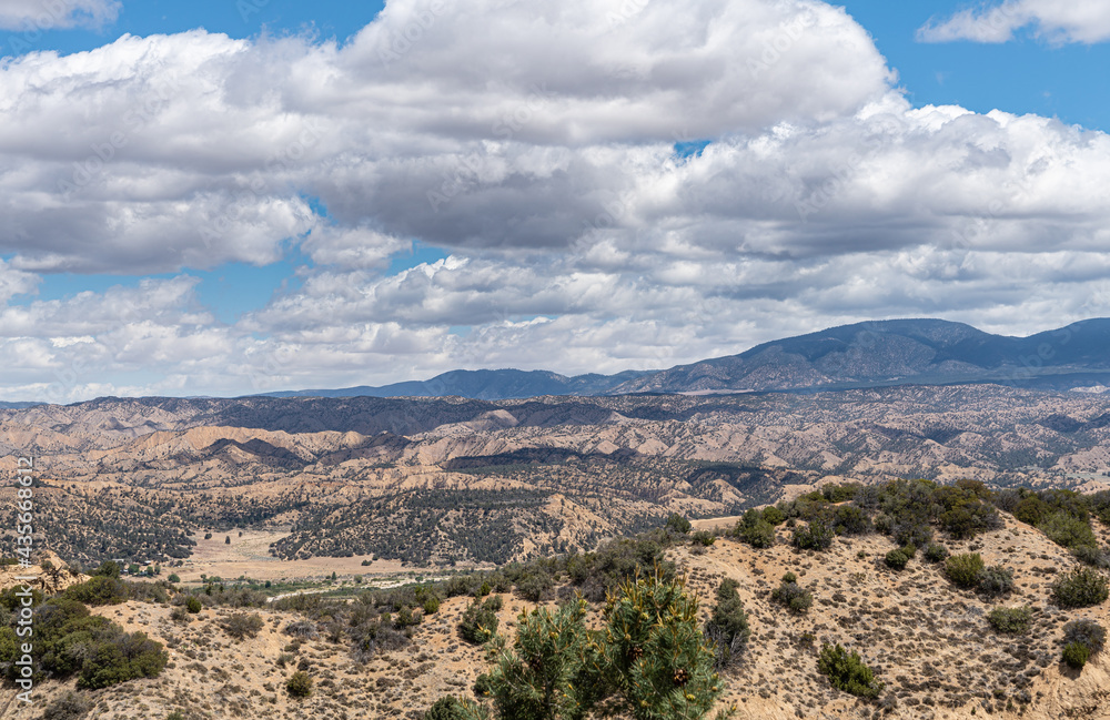 Los Padres National Forest, CA, USA - May 21, 2021: Heavy blue cloudscape over park east side wide scenery.  Beige brown naked rocks and green shrub sprinkled all over.