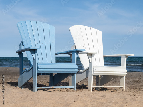White and blue Adirondack chairs on a sandy beach on a sunny day