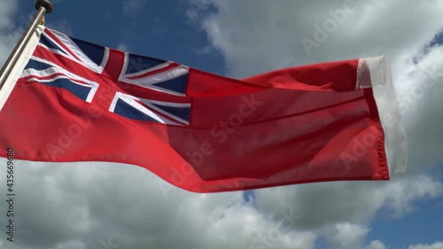 Close up of red ensign flag flying in the wind against a blue sky filled with fluffy white clouds. Ship flag representing united kingdom of Great Britain and Ireland. Slow motion footage flag in wind
