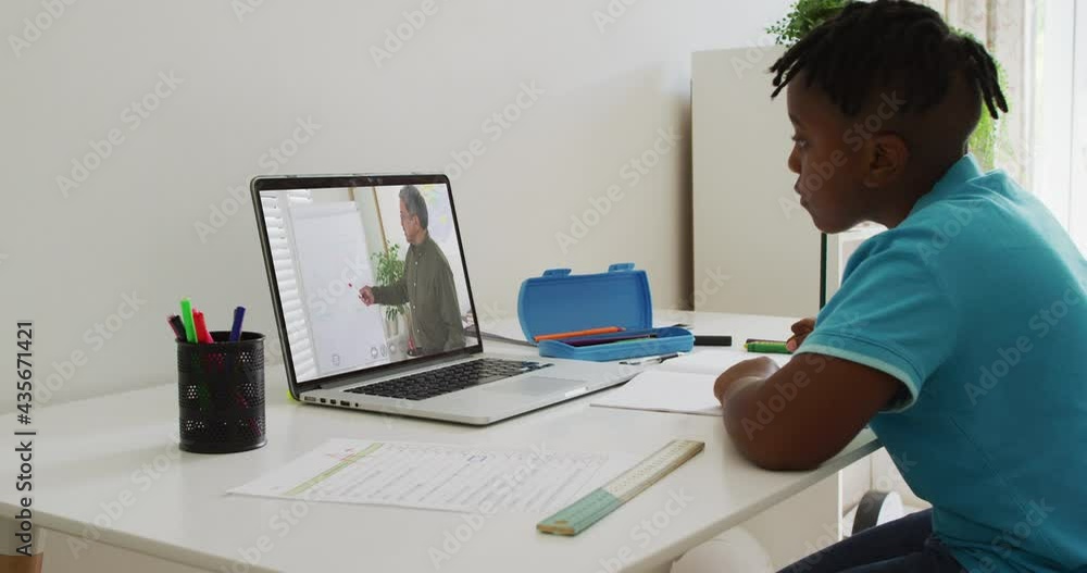 African american boy doing homework while having a video call with male teacher on laptop at home African american boy doing homework while having a video call with male teacher on laptop at home
