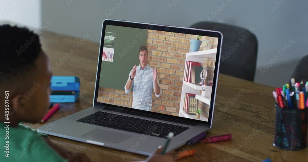 African american boy doing homework while having a video call with male teacher on laptop at home African american boy doing homework while having a video call with male teacher on laptop at home
