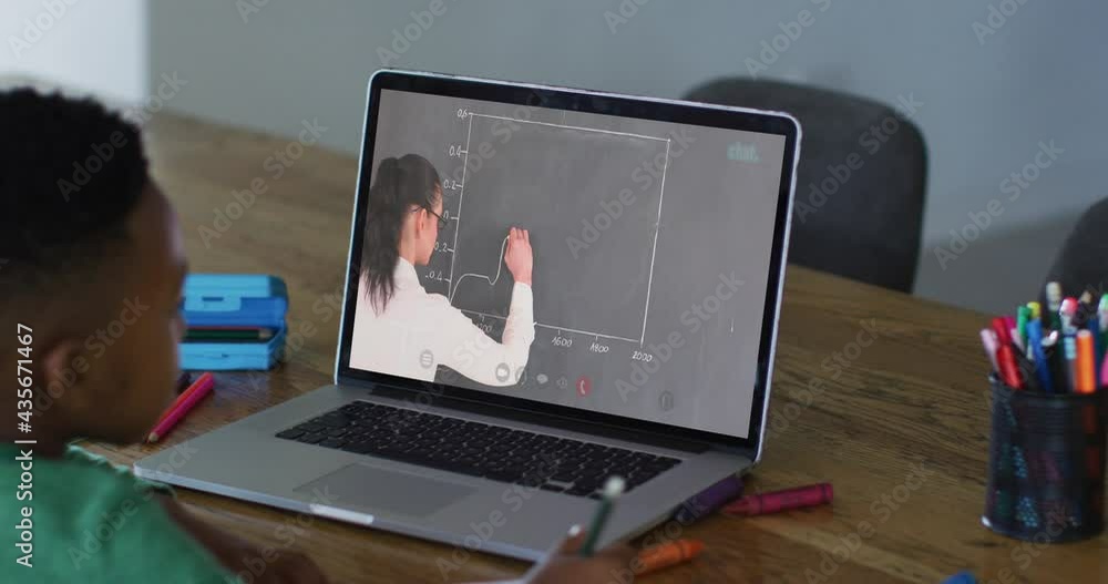 African american boy doing homework while having a video call with female teacher on laptop at home African american boy doing homework while having a video call with female teacher on laptop at home
