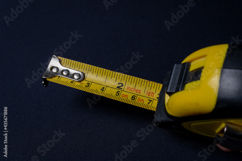 Yellow measuring tape with black accents on a dark background. Used for measurements at home and in the professional environment for correct marking. Detail for measurements marked in red.