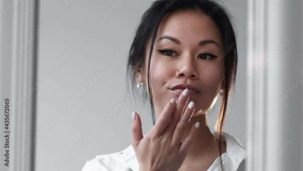 Beautiful asian woman. Trend makeup. Stylish look. Fashion model. Elegant sensual lady with accent black eyeliner applying pastel glossy lipstick in light room interior.
