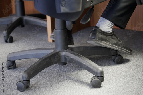 The legs of an office clerk or dispatcher on duty sitting on a pneumatic chair with wheels. Concept of office furniture and its use. Selective focus