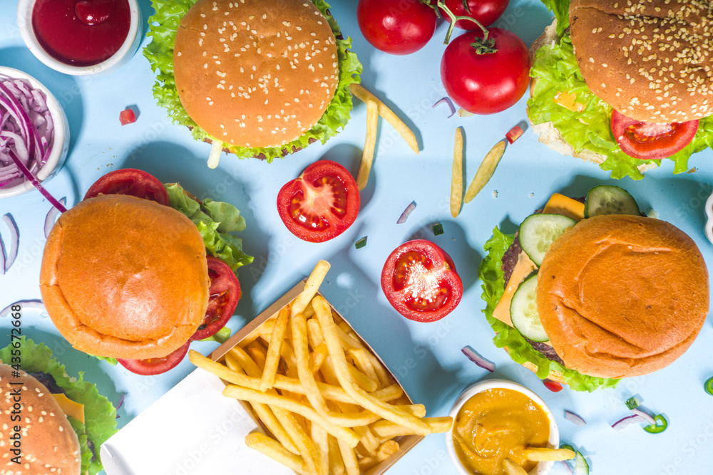 Fastfood, burger party concept. Various delicious burgers set with french fries and sauces on bright blue background flatlay top view copy space Fastfood, burger party concept. Various delicious burgers set with french fries and sauces on bright blue background flatlay top view copy space