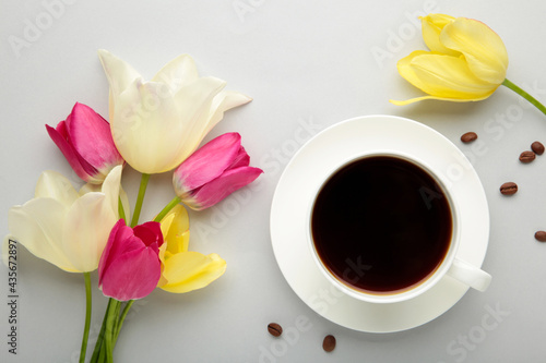 Cup of coffee with tulips on grey background