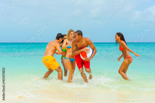 Young people at the beach, dressed in bathing suits, bikinis, playing with beach ball, interracial, black