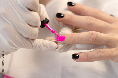 Manicure  covering the natural nails of a young girl with a bright pink gel polish in a beauty salon by a specialist. Close-up. The concept of professional nail care.