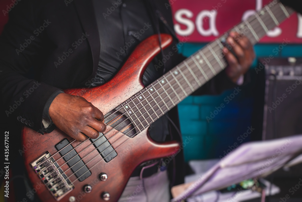 Concert view of an african-american musician with electric bass guitar player during band performing rock music,  bassist player on stage