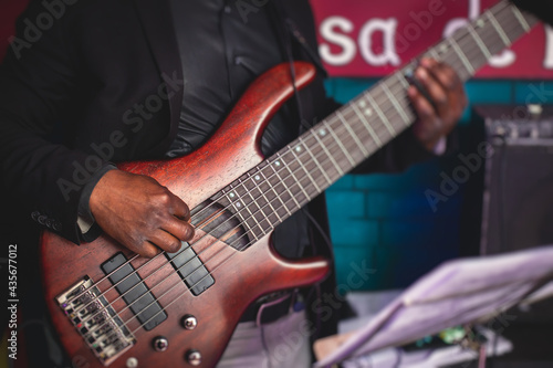 Concert view of an african-american musician with electric bass guitar player during band performing rock music, bassist player on stage