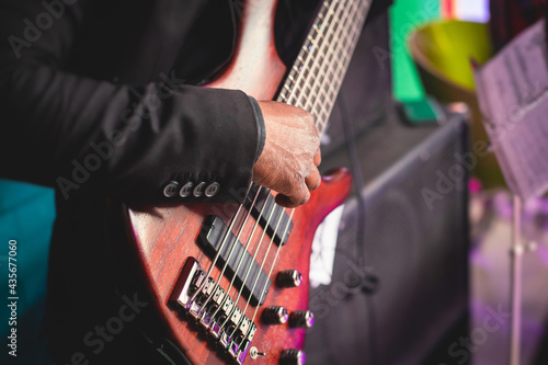 Concert view of an african-american musician with electric bass guitar player during band performing rock music,  bassist player on stage photo